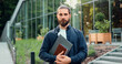 © serg - Business man in glasses smiling on camera while standing outdoors by modern office building. Portrait of positive male person dressed in stylish formal clothes