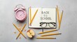 © Veayo - A pink alarm clock, open notebook with the words 'Back to School' written on it, and scattered pencils on a grey background.