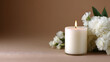 © Sakda - Single white candle with white flowers on a warm brown background, creating a calm elegant still life with soft light and peaceful decorative atmosphere.
