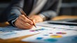 © Pug - A close-up view of a professional analyzing colorful charts and graphs on paper. The individual uses a pen to highlight data, showcasing a focus on strategy and insights.