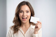 © Meow Creations - Cheerful young woman holding a blank white plastic card while smiling happily at the camera