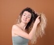 © New Africa - Unhappy woman trying to brush her tangled hair on brown background