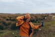 © SHOTPRIME STUDIO - Young woman lifestyle outdoors takes selfie with smartphone in autumn field wearing orange jacket and hat. Casual fashion and nature concept with relaxed mood and natural light.