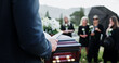 © peopleimages.com - Person, hands and funeral with holy bible or coffin for memorial service, prayer or worship of god. Family, people or christianity with book, religion or faith at graveyard or cemetery for death