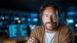 © svastix - A focused man with curly hair and glasses smiles in a dimly lit modern workspace, highlighting the blend of technology and human connection in today’s work environment.