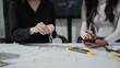 © NanSan - Architects collaborate over building floor plans, using compass and phone at modern office desk with measuring tools, focused teamwork and planning concept.