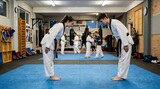 Young martial arts students bowing wearing white gi and black belts in dojo
