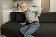 © brizmaker - Elderly man experiencing severe back pain while sitting on sofa