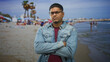 © Krakenimages.com - Hispanic man with glasses and beard, arms crossed showing closed posture in studio with beach backdrop; defiance.