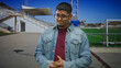 © Krakenimages.com - Man with beard and glasses adjusts glasses while clasping hands in front of a sports building by a soccer goal and stadium bleachers; curiosity.