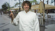 © Krakenimages.com - Hispanic man chef in white jacket points index finger upward and smiles beside outdoor cafe tables and umbrellas on a busy street; cheerful hospitality.