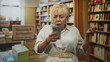 © Krakenimages.com - Senior hispanic woman holds smartphone and frowns with hand on hip in bookstore; digital confusion help.