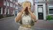 © Krakenimages.com - Woman with yellow glasses holds cheeks with both hands and sticks out tongue on cobbled street; surprise playful curiosity.