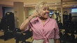 © Krakenimages.com - Senior woman making hand phone gesture while smiling, wearing red striped shirt in gym; playful connection joy.