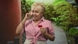 © Krakenimages.com - Senior hispanic woman points finger and holds a small red heart on a building walkway among greenery; affection invitation.