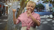 © Krakenimages.com - Woman with finger to lips for silence on a street, thumb pointing behind her and striped shirt visible; playful mischief.