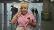 © Krakenimages.com - Senior woman holding a small red heart covers mouth yawning while waiting in an airport terminal with blurred travelers and bins visible; fatigue solitude.