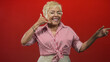 © Krakenimages.com - Senior hispanic woman points finger and makes phone hand gesture showing hand and smile in a studio; joyful connection.