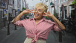 © Krakenimages.com - Senior hispanic woman flashes v sign with both hands near face, smiling, wearing red striped tied shirt and white glasses on a narrow street; joyful playfulness.