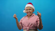 © Krakenimages.com - Woman wearing santa hat and glasses points finger and raises fists in studio blue backdrop; holiday joy.
