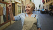 © Krakenimages.com - Senior hispanic woman in apron smiling points finger upward at storefront on cobblestone street; friendly confidence.