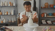 © Krakenimages.com - Young chinese artisan man brushes glaze onto glossy white ceramic vase on rotating pottery wheel in studio; focus.