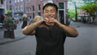 © Krakenimages.com - Smiling man forming heart gesture with hands in urban pedestrian street scene with blurred passersby; love.