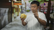 © Krakenimages.com - Young chinese man holds a clear glass bowl of potato chips with both hands on street under midday sunlight; curiosity craving.