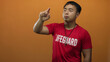 © Krakenimages.com - Man lifeguard points finger to object in studio against vivid orange backdrop; vigilance readiness protection safety.