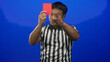 © Krakenimages.com - Young male chinese referee holds red card, blows whistle and points finger in blue studio; authority.
