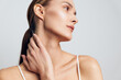 © SHOTPRIME STUDIO - Young woman with smooth skin and natural makeup touches her neck gently, looking sideways with calm expression against a plain light background, showcasing beauty and skincare concept.