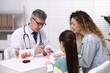 © New Africa - Endocrinologist in glasses checking little girl's blood sugar level with lancet pen while her mother supporting her at white desk in clinic
