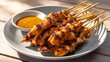 © Reandz - Pile of grilled chicken satay skewers served with spicy peanut dipping sauce on wooden table for Asian appetizer