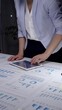 © rogerphoto - Professional businesswoman working at a desk surrounded by financial reports, charts, and graphs, focusing on data analysis to develop strategic plans and improve performance