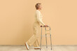 © Pixel-Shot - Mature woman using walker near beige wall