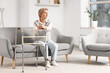 © Pixel-Shot - Mature woman with walker sitting on sofa at home