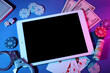 © Pixel-Shot - Tablet computer with poker chips, money and handcuffs on table in casino, closeup
