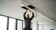 © Masaji - A male electrician standing on a ladder carefully installs a long modern LED light fixture into the ceiling of a new office space.