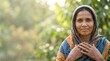 © Mariya Sorvacheva - South Asian woman wearing colorful scarf stands outdoors, smiling gently with hands clasped, surrounded by lush greenery, representing resilience and hope in migration
