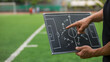 © Naufal - Soccer coach holding chalkboard tactics board, explaining strategy and formation during training session, highlighting teamwork, planning, and game analysis.