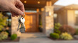 © Foxy Sight - Hand holding house keys with a house-shaped keychain against a blurred background of a new modern suburban home. Real estate concept.