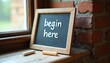 © Maryna - Chalkboard with text begin here sits on rustic shelf by window. Two chalk sticks rest near board. Brick wall background. Inspirational message.
