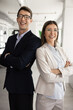 © fizkes - Young male and female business duo, startuppers standing together in modern office, smiling and crossing their arms, exuding professionalism, success and unity. Business partnerships and perspectives