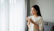 © ChimE - Serene Moment: A Young Woman Enjoying a Beverage by the Window. A young woman in a cozy setting, enjoying a warm drink while gazing out of a window. capturing a moment of serenity and tranquility.