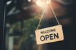 © AnupKumar - Wooden welcome open sign hanging on glass door of store or boutique with blurred interior background