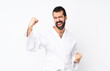 © luismolinero - Young man doing karate over isolated white background celebrating a victory