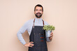 © luismolinero - Man holding a plant over isolated background posing with arms at hip and smiling