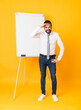 © luismolinero - Full-length shot of businessman giving a presentation on white board over isolated yellow background looking far away with hand to look something
