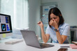 © Tj - Young Asian business woman feeling tired, rubbing aching eyes from prolonged computer screen use, showing work related stress, exhaustion, and burnout in a modern office setup