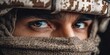 © NovaVision - Close-up of a soldier's intense eyes peering through a desert camouflage helmet and scarf